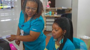 Two healthcare workers in blue scrubs looking at a computer screen.