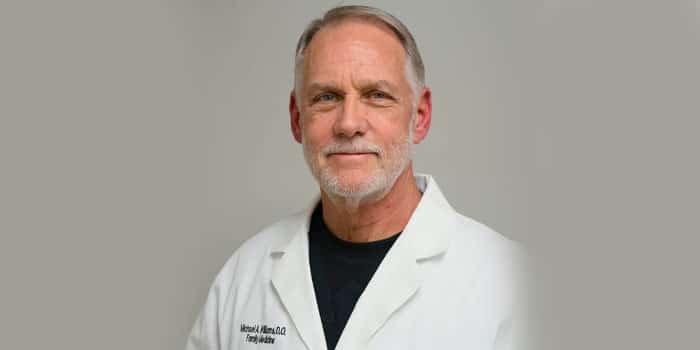A man in a white lab coat, smiling at the camera.